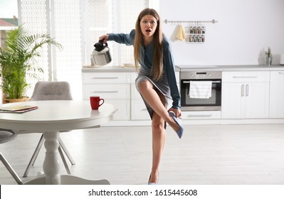 Young woman pouring coffee into cup while putting on shoes at home in morning Foto stock