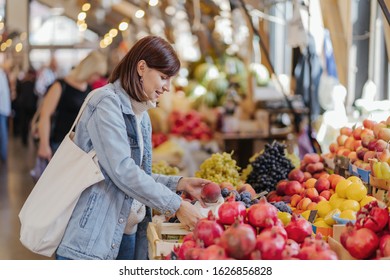 Стоковая фотография: Young Woman puts fruits and vegetables in cotton produce bag at food market. Reusable eco bag for shopping. Sustainable lifestyle. Eco friendly concept. 