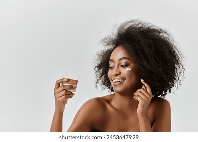 A young African American woman with curly hair smiles while holds a cream jar, radiating joy and contentment. Arkivfotografi