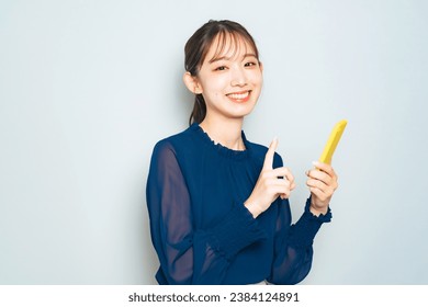 A young Asian woman holding a smartphone and smiling. 库存照片