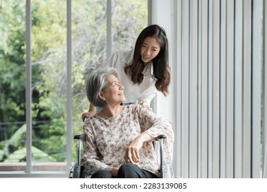 Young Asian woman nurse taking care senior elderly woman patient with careful on wheelchair. Happy smiling female caring senior old woman on wheelchair with kindly in nursing home 库存照片