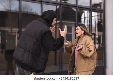 Стоковая фотография: Young arguing sad couple two friends family man woman in casual clothes screaming scolding together walking outdoor near glass office. Woman yelling at man. Couple arguing, having relationship problem