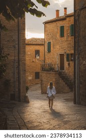 A young blonde female tourist explores backstreets of the quaint and charming Tuscan village Monticchiello, Tuscany, Italy. Foto stock