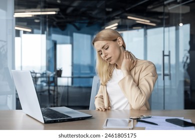 オフィスの机でノートパソコンを操作しているときに首の痛みを感じる若い女性実業家。仕事上のストレスや不快感の概念。の写真素材