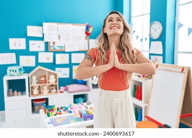 Young caucasian woman working as teacher at kindergarten begging and praying with hands together with hope expression on face very emotional and worried. begging. : stockfoto