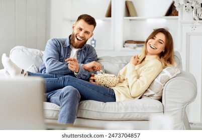 Young Couple Laughing Watching Comedy Movie Online And Eating Popcorn Foto stock