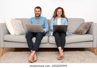 Стоковая фотография: Young couple sitting on sofa at home and uses laptops. Online shopping, booking, banking.