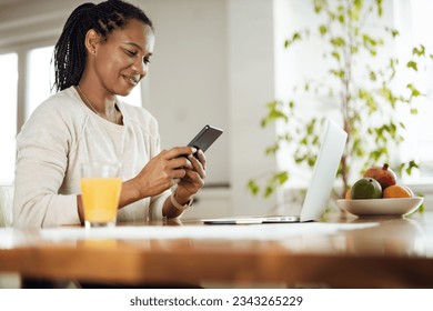 Young happy black woman using cell phone while working from home. స్టాక్ ఫోటో