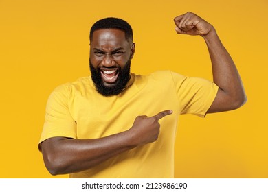 Young happy black man 20s wearing bright casual t-shirt point finger on biceps muscles on hand demonstrating strength power isolated on plain yellow color background studio. People lifestyle concept 库存照片
