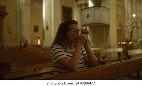 A young hispanic woman is seen praying inside a beautiful italian church, providing a serene religious ambiance.: stockfoto