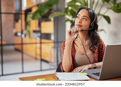 Young latin business woman wearing headphones with microphone daydreaming while working on laptop. Thoughtful mixed race businesswoman take a break and thinking about new idea.  Adlı Stok Fotoğraf