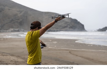 A young Latin man prepares to fly a drone on a sunny beach, capturing the scenic ocean view Arkistovalokuva
