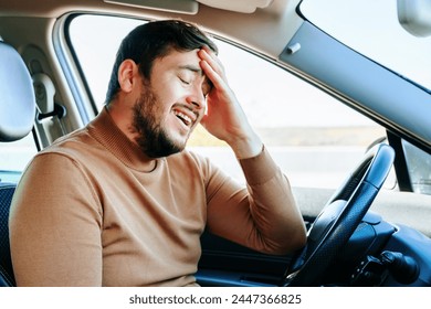 Un joven se sienta al volante en un coche con los ojos cerrados, sonriendo cansadamente, frotándose la frente con la mano. El camino era largo y difícil. El tipo está descansando. Personas y emociones. Foto de stock