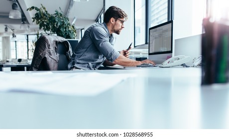 Young man sitting in office and working on desktop pc. Businessman looking at computer monitor while working in office. स्टॉक फ़ोटो