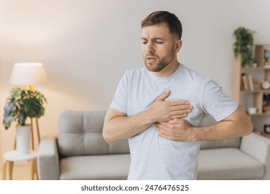 A young man is standing at home and holding his chest. Feels severe pain, shortness of breath, panic attack, heart attack, stroke. Foto stock