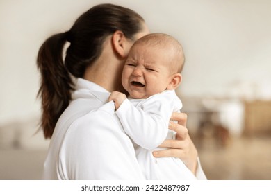 Young mother holding crying newborn baby girl or boy, calming kid, lullying in bedroom interior , focus on baby, free space Foto Stock