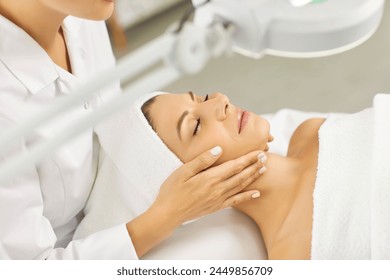Young professional woman cosmetologist doing skin care facial treatment examining its condition for female client with lamp in beauty clinic. Cosmetology and beauty procedure concept. Stockfotó