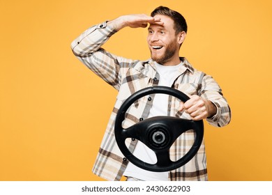 Стоковая фотография: Young smiling happy Caucasian man wear brown shirt casual clothes hold steering wheel driving car look far away distance isolated on plain yellow orange background studio portrait. Lifestyle concept