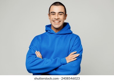 Young smiling happy cheerful middle eastern man he wears blue hoody casual clothes hold satisfied hands crossed folded look camera isolated on plain solid white background studio. Lifestyle concept Foto stock