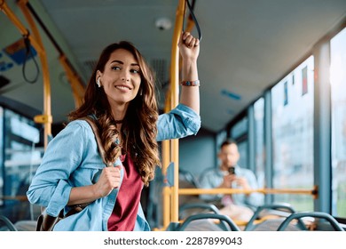 Young smiling woman holding onto a handle while traveling by public bus. Stockfoto