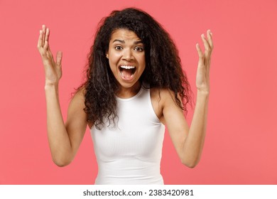 Young stressed furious nervous irritated angry woman of African American ethnicity she wear casual white tank shirt spreading hands scream shout isolated on pink background. People lifestyle concept Stock fotografie