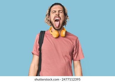 Joven estudiante con mochila y auriculares divertidos y amistosos sacando la lengua. Foto de stock