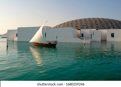 Abu Dhabi / UAE - January 3, 2019: Louvre museum in Abu Dhabi. View of beautiful Louvre exterior with waterfront and wooden sailboat. 에디토리얼 스톡 사진