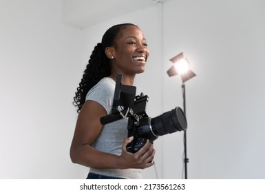 African American Female Videographer Posing with Video Camera in Hand on Film Set. Camera Woman is Proud and Smiling Looking Off Camera. Foto stock