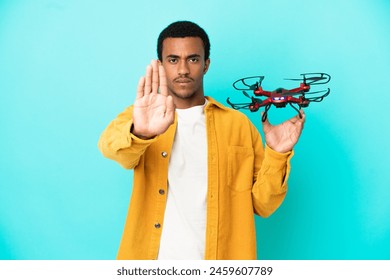 African American handsome man holding a drone over isolated blue background making stop gesture Arkistovalokuva