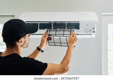Air conditioner maintenance. Male technician repairs home climate system in living room. Man is cleaning filters of conditioner 库存照片