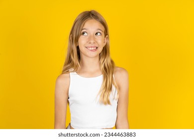 黄色い背景に白いTシャツを着た白人の女の子が驚いて唇を噛んで、空のスペースにトリッキーに見える。の写真素材