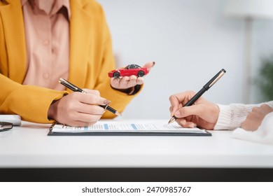 Asian businesswoman and a salesman discuss car sales, insurance, and financing with a customer at a desk, covering used car loans, premiums, deductibles, and various insurance coverage options. 庫存照片