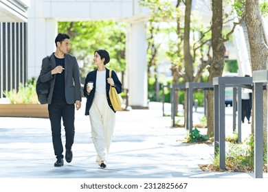 Una pareja asiática camina por una elegante calle rodeada de vegetación. Foto de stock