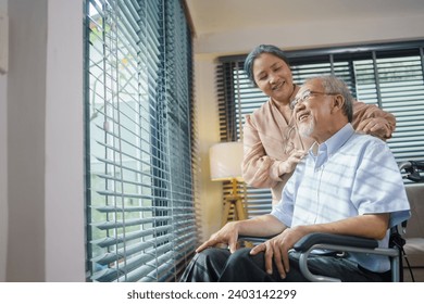 Asian grandmother giving a massage to grandfather sitting on wheelchair at home. Wife takes care of her patient husband. Retired couple sharing love and bonding. Healthcare insurance concept 库存照片