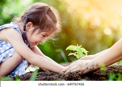 Asian little girl and parent planting young tree on black soil together as save world concept in vintage color tone Stock Photo