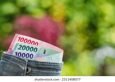 アジア人男性の手がルピア紙幣で満たされた財布を持つ(Rp 10,000、Rp 20,000、Rp 100,000):男性は、ぼかした自然の背景に変化を与えているか、何かに支払っているの写真素材