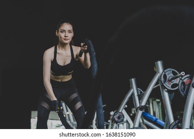 asian powerful strong woman slim body training with battle rope in cross at fitness gym with machine in dark background, exercise, bodybuilder, lifestyle, exercise fitness, workout and sport concept Foto stock