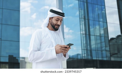 Arab businessman with high-rise buildings with glass windows as background. Arabic Man in Kandura Thobe Thawb for Middle Eastern corporate finance banking concept Arkistovalokuva