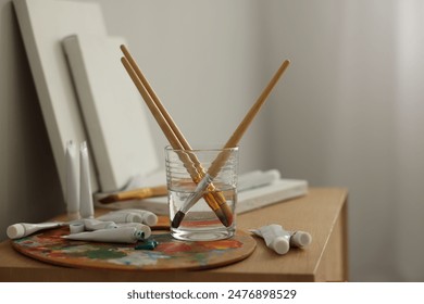 Artist's palette, brushes in glass of water and paints on wooden table indoors स्टॉक फ़ोटो