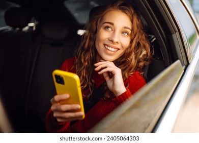 차 뒷좌석에 휴대폰을 들고 있는 매력적인 여자. 전화기를 손에 들고 있는 젊은 여성이 택시를 타면서 문자를 보내고 있다. 교통, 기술 라이프스타일 스톡 사진