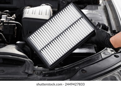 Auto mechanic holds car air filter in his hands near engine compartment, close-up. Concept of replacing auto parts, replacing air filter, car maintenance, protection from allergens, dirt,soot, viruses 库存照片