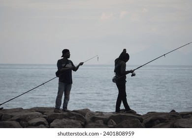 2023年12月17日バンダアチェ：海を背景に岩の上を釣り竿を持って歩く2人のエディトリアル写真素材