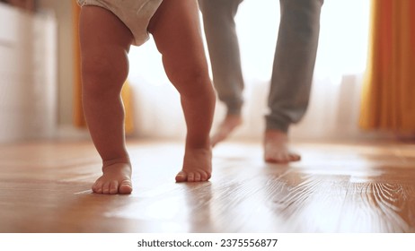 baby first steps. happy family kid dream concept. father teaches baby daughter to take first steps at home in front of window. lifestyle father's day concept. baby takes his first steps 库存照片