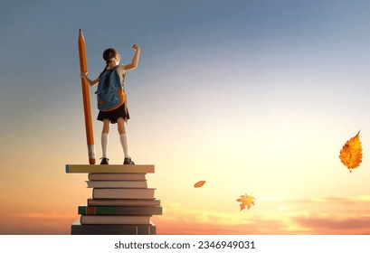 Back to school! Happy cute industrious child standing on the tower of books and holding a huge pencil on background of sunset sky. Concept of education and reading. The development of the imagination., fotografie de stoc