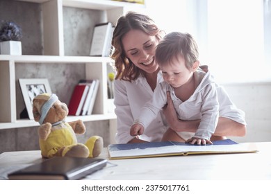 スーツを着た美しいビジネスマンのお母さんは、かわいい男の子と一緒に本を読んで、家で微笑んでいますの写真素材