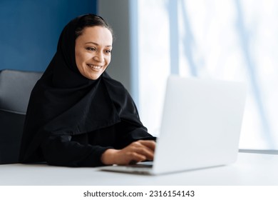 Beautiful woman with abaya dress working on her computer. Middle aged female employee at work in a business office in Dubai. Concept about middle eastern cultures and lifestyle Arkistovalokuva