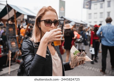 Beautiful young woman holding delicious organic salmon vegetarian burger and drinking homebrewed IPA beer on open air beer an burger urban street food festival in Ljubljana, Slovenia Stock fotografie