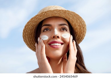 Beautiful Young woman with sun cream on face. Girl holding sunscreen bottle on the beach. Female in hat applying moisturizing lotion on skin.Skin care. Sun protection. Suntan: stockfoto