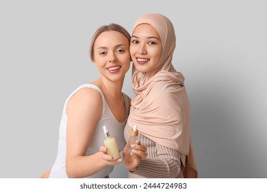Beautiful young women with bottles of cosmetic oil on grey background Stockfotó
