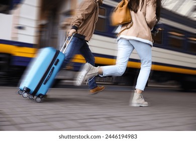 Being late. Couple with suitcase running after train on station, closeup. Motion blur effect Foto stock